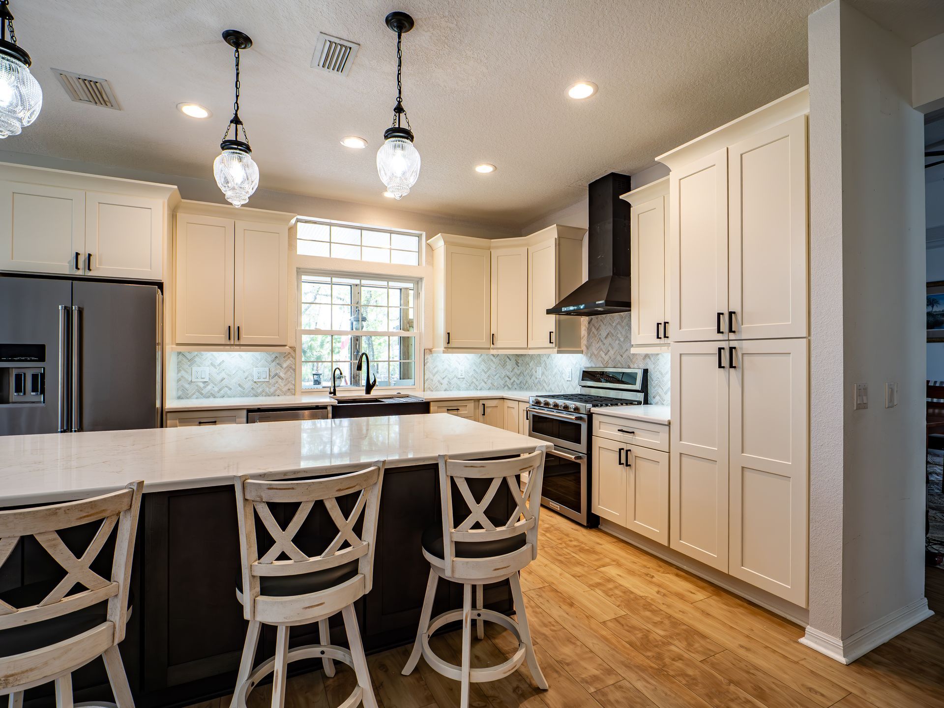Cream-colored kitchen with dark island and cabinets. Pendant lights over island with bar stools.