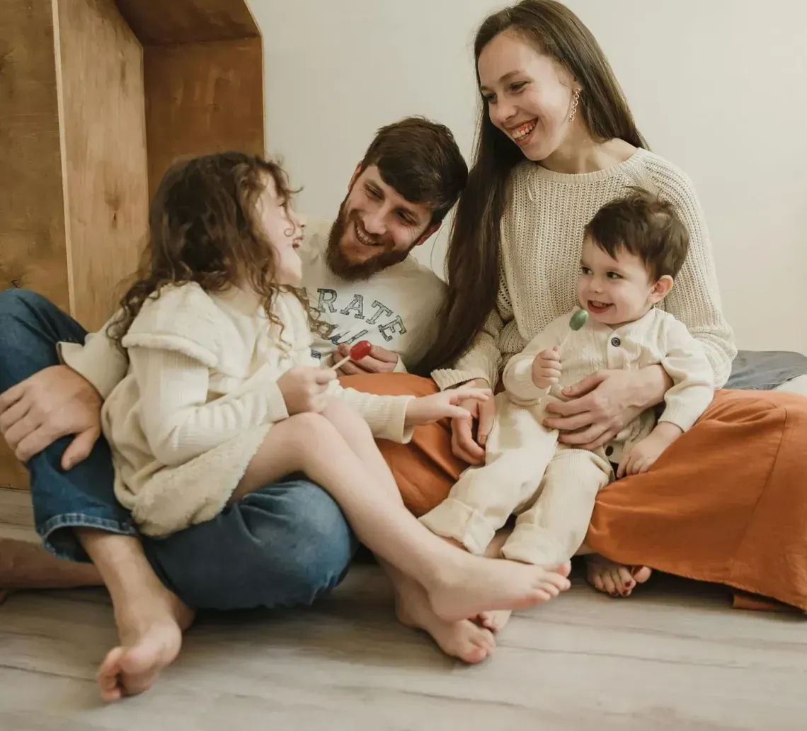 Family sitting on the floor, smiling and cuddling in a cozy living room.