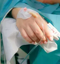 Hand with IV line and bandage resting on white blanket in a hospital setting
