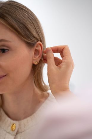 Woman adjusting a gold hoop earring, wearing a white top against a light background
