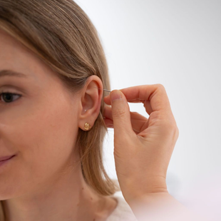 Woman adjusting a gold hoop earring, wearing a white top against a light background