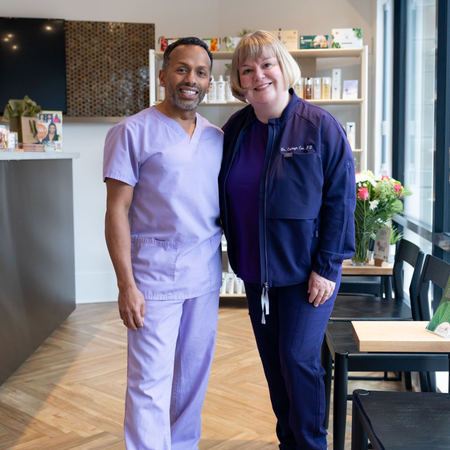 Two staff members in purple scrubs smiling in a bright clinic waiting area