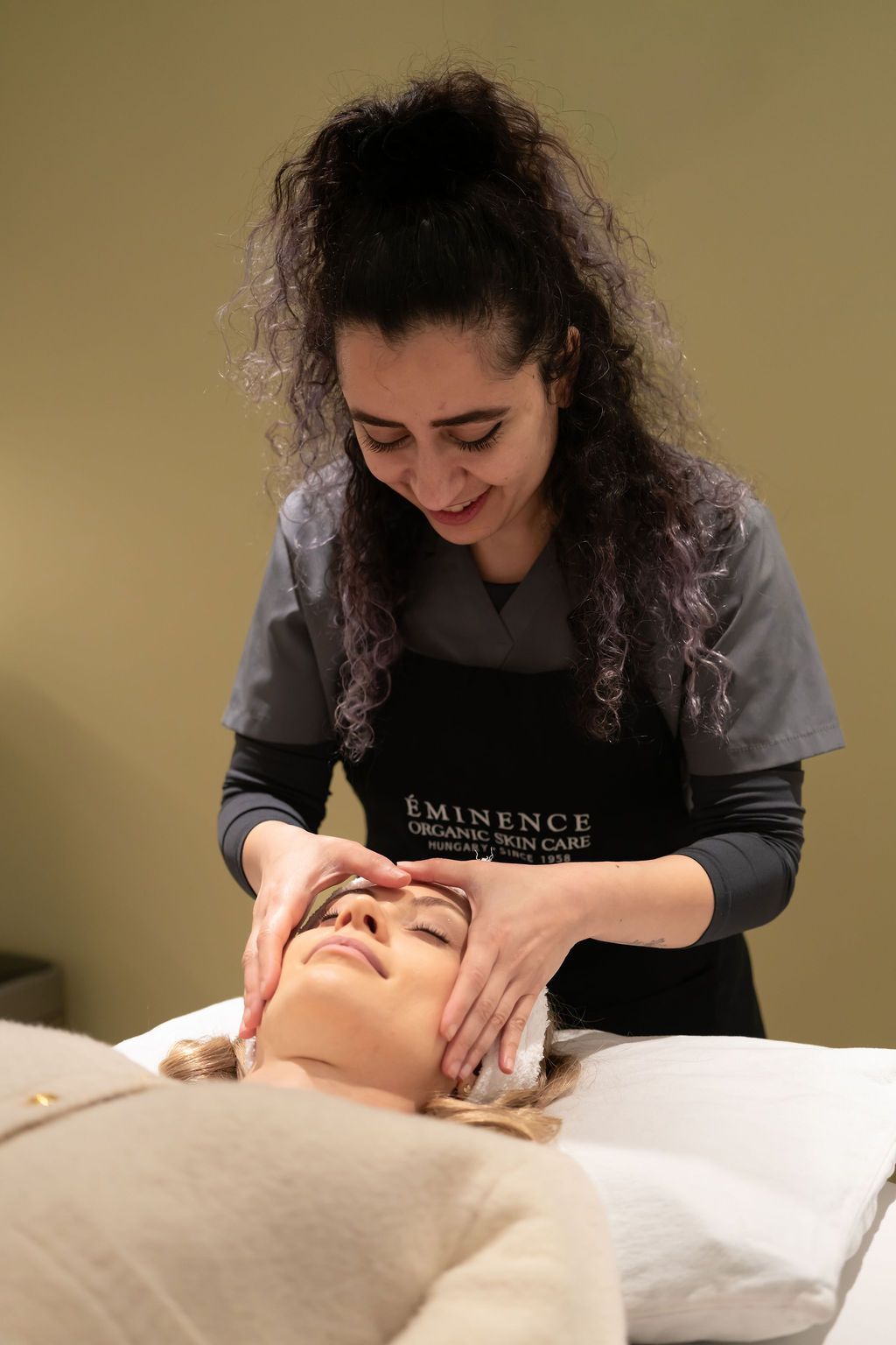 Massage therapist giving a facial treatment to a reclining client in a spa setting