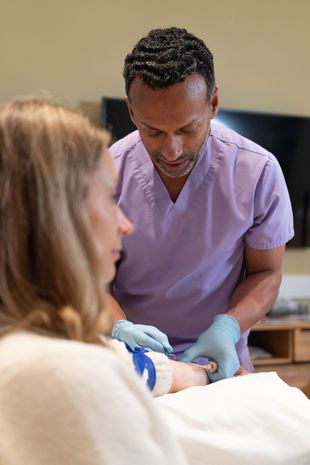 Healthcare worker in purple scrubs and gloves tending to a patient in a clinical setting