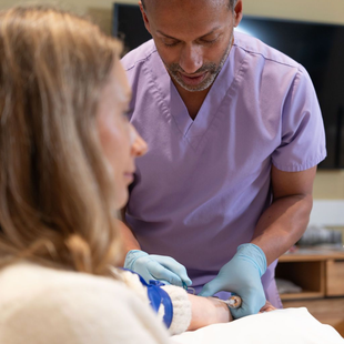 Healthcare worker in purple scrubs and gloves tending to a patient in a clinical setting