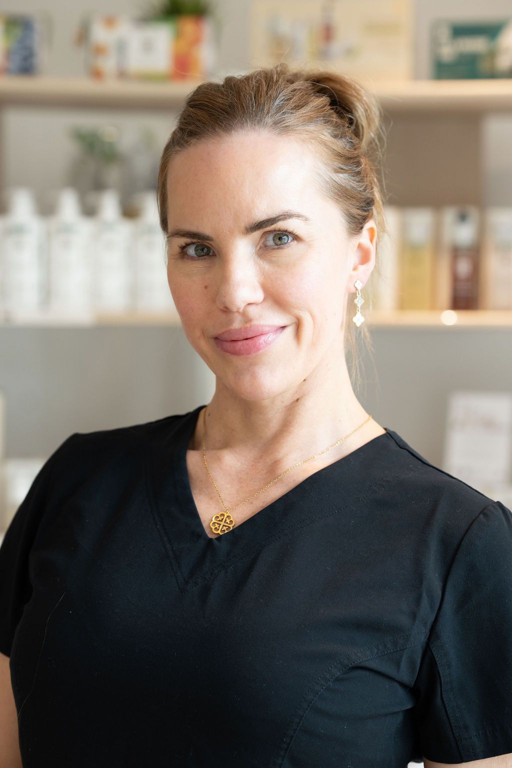 Woman in a black top smiling in a softly lit office or salon setting.