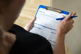 Person filling out a form on a blue clipboard with a pen.
