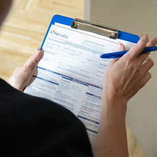 Person filling out a form on a blue clipboard with a pen.