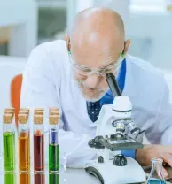 Scientist examining a sample through a microscope beside colorful test tubes in a lab