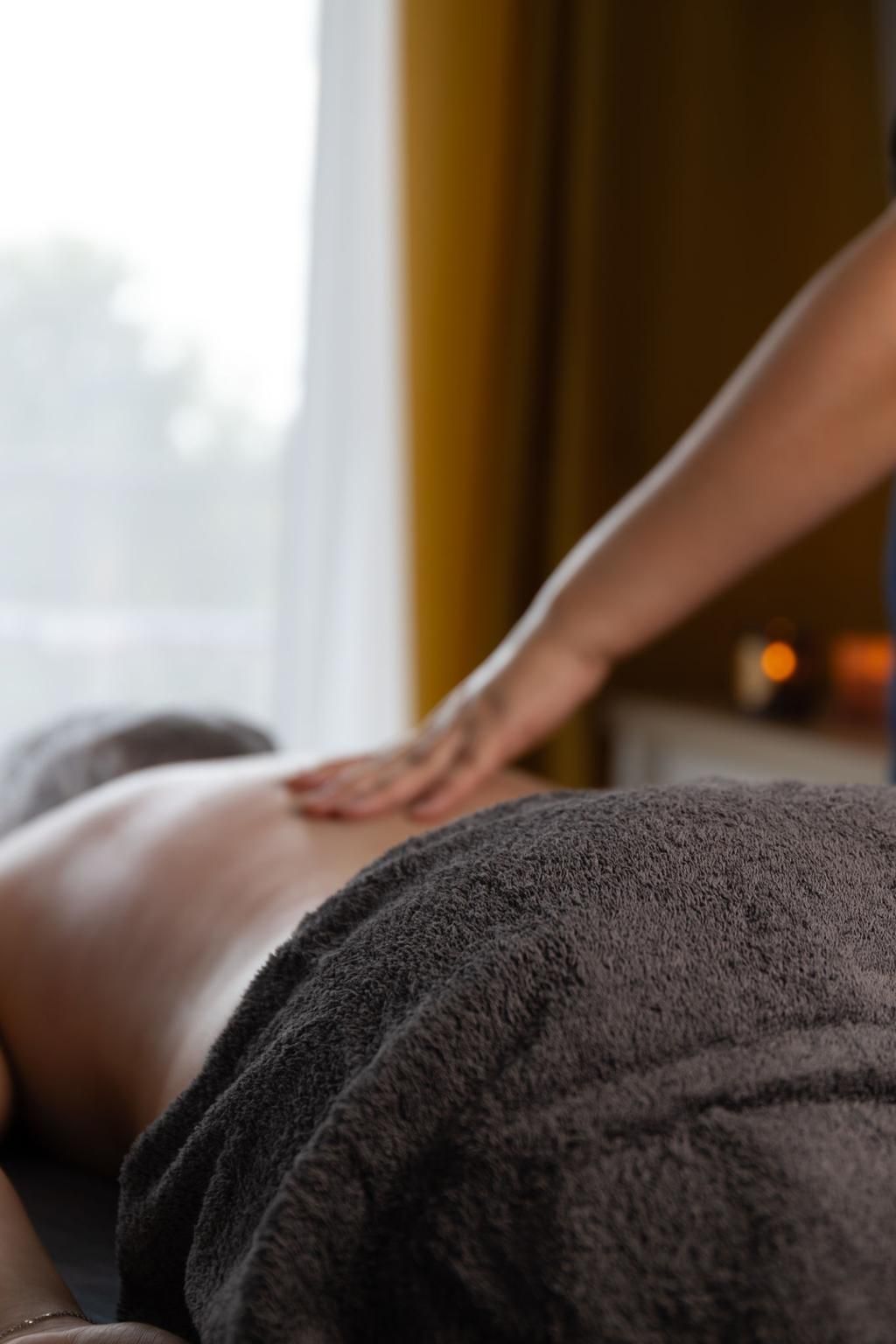 Massage therapist rubbing a person’s back with a towel in a dim spa room