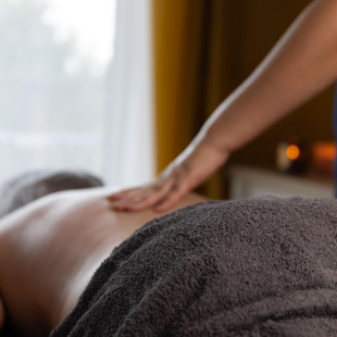 Massage therapist rubbing a person’s back with a towel in a dim spa room