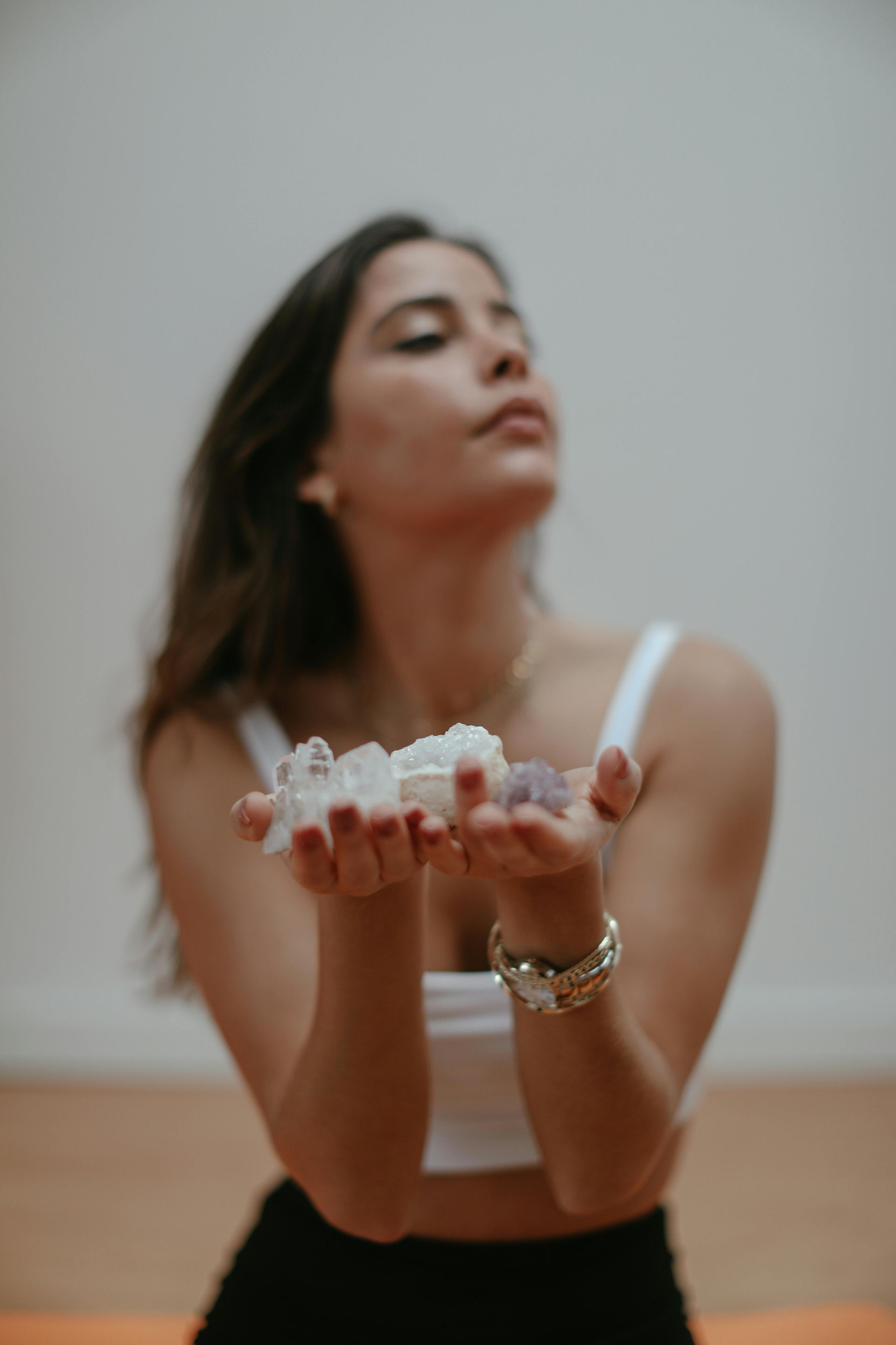 Woman kneeling and holding white flower petals in cupped hands against a soft gray background