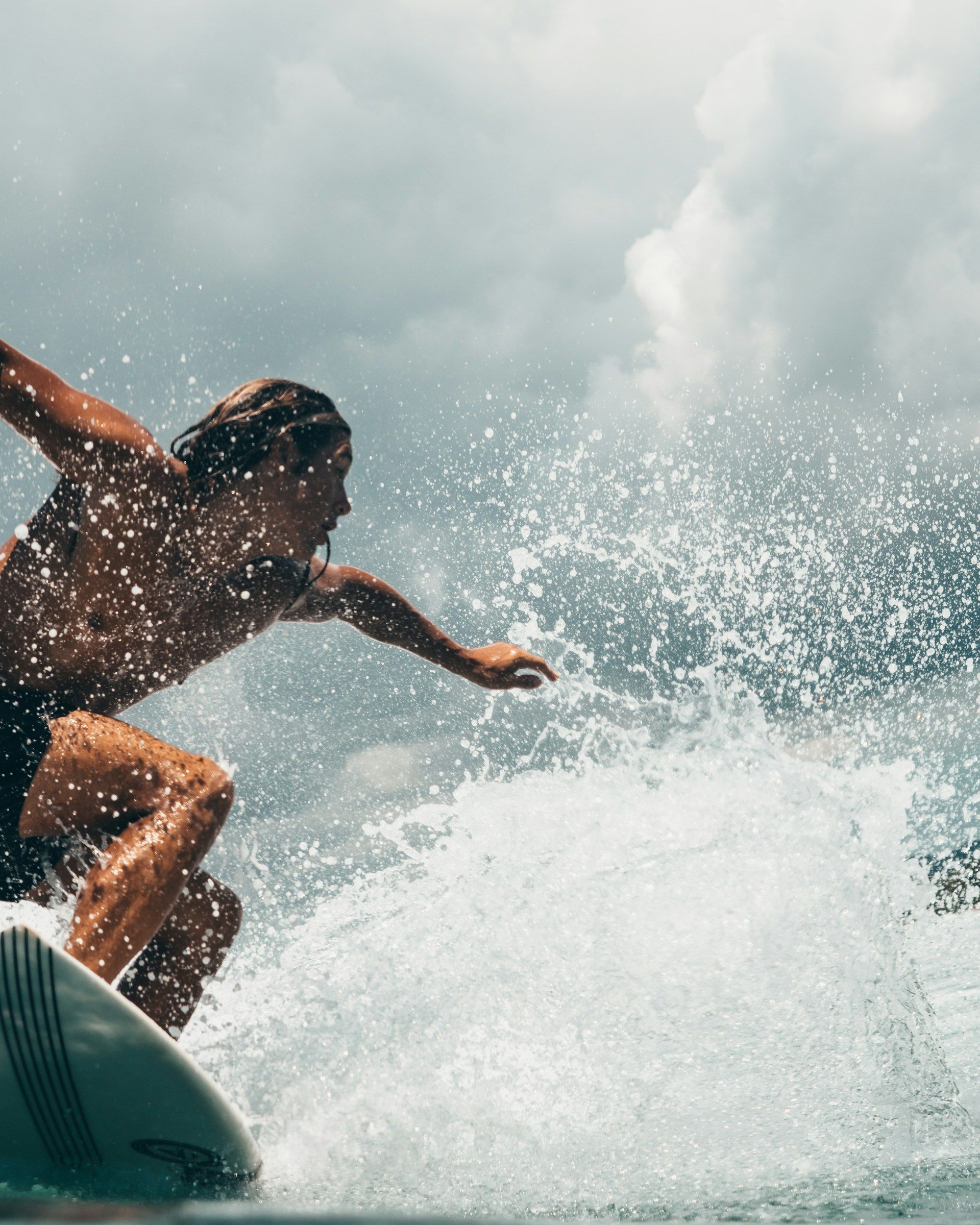 Surfer riding a wave, arms outstretched, water splashing. Overcast sky.