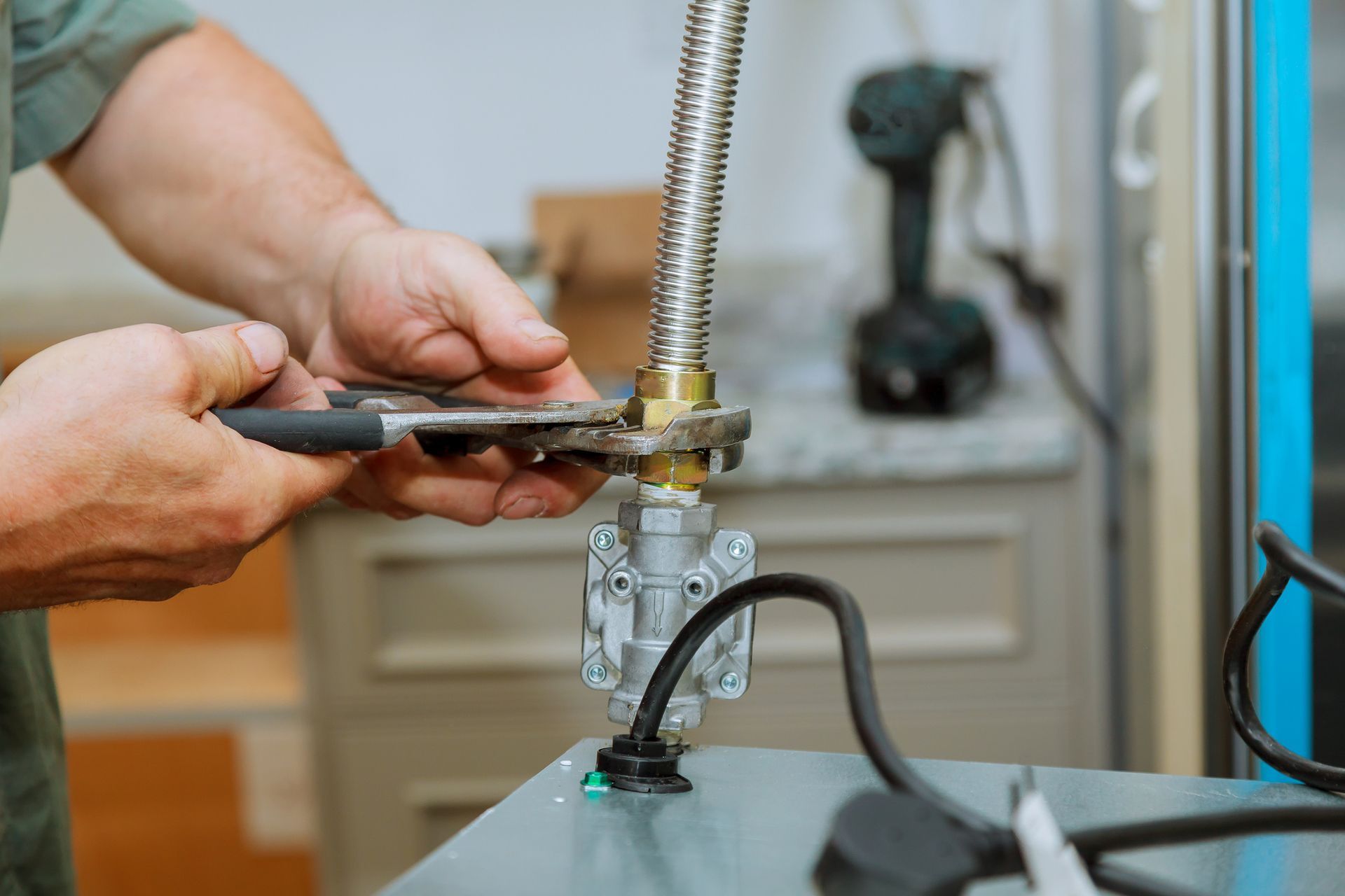 Close-up of a pair of hands as a person uses a pair of pliers on an oven’s gas hob inside a kitchen.