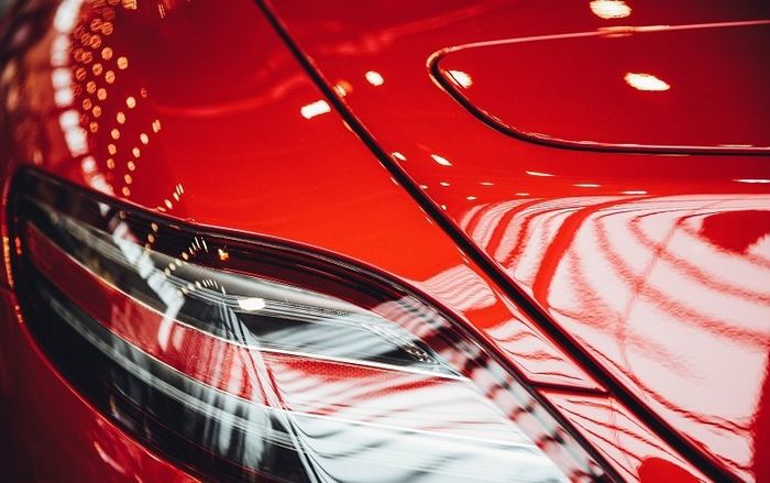 Close-up of a red car’s front headlight and glossy hood