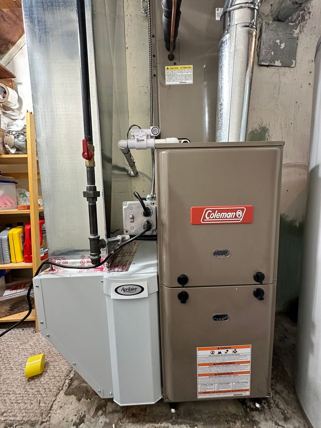 Furnace with Coleman logo installed in a basement, pipes and ductwork visible.