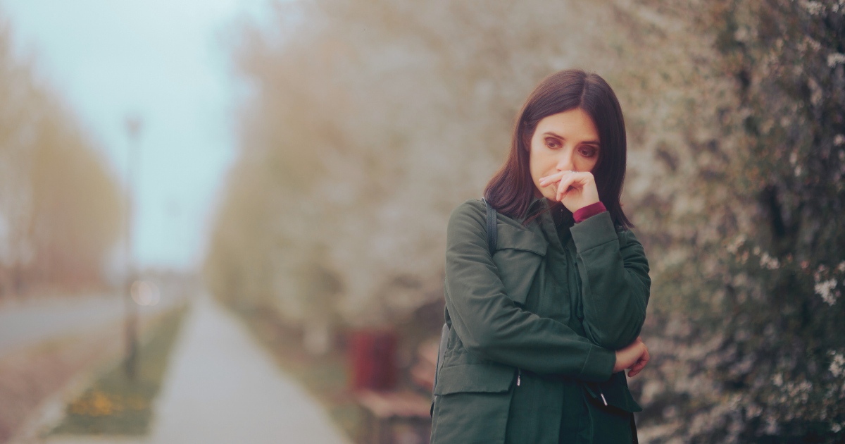 a woman stands on a path in a park looking sad and uncertain