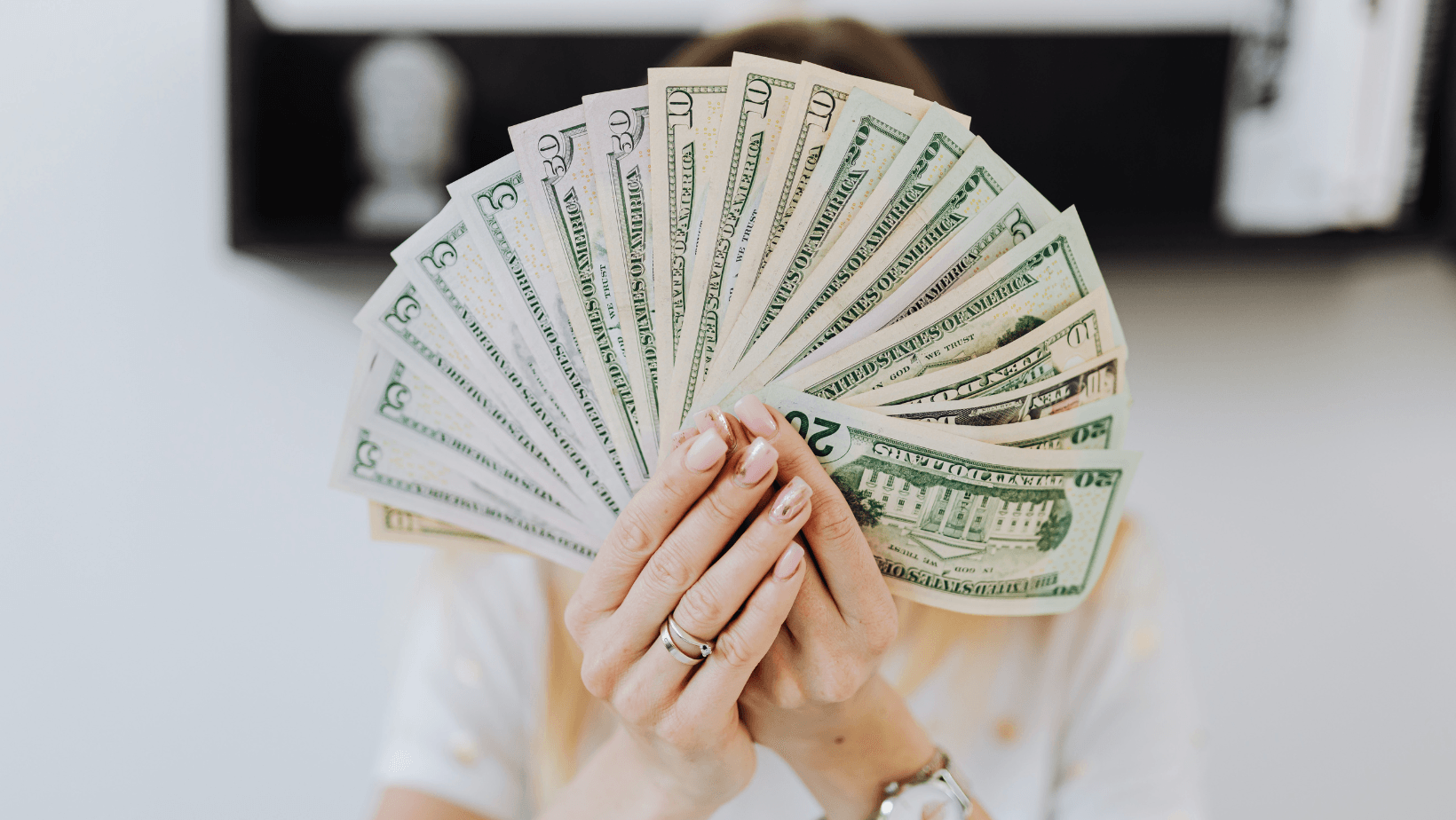 A woman is holding a fan of money in front of her face.