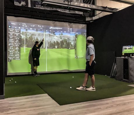 A man and a woman are playing golf in a simulator.