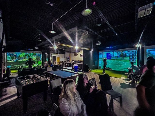 A row of golf simulators are lined up in a warehouse.