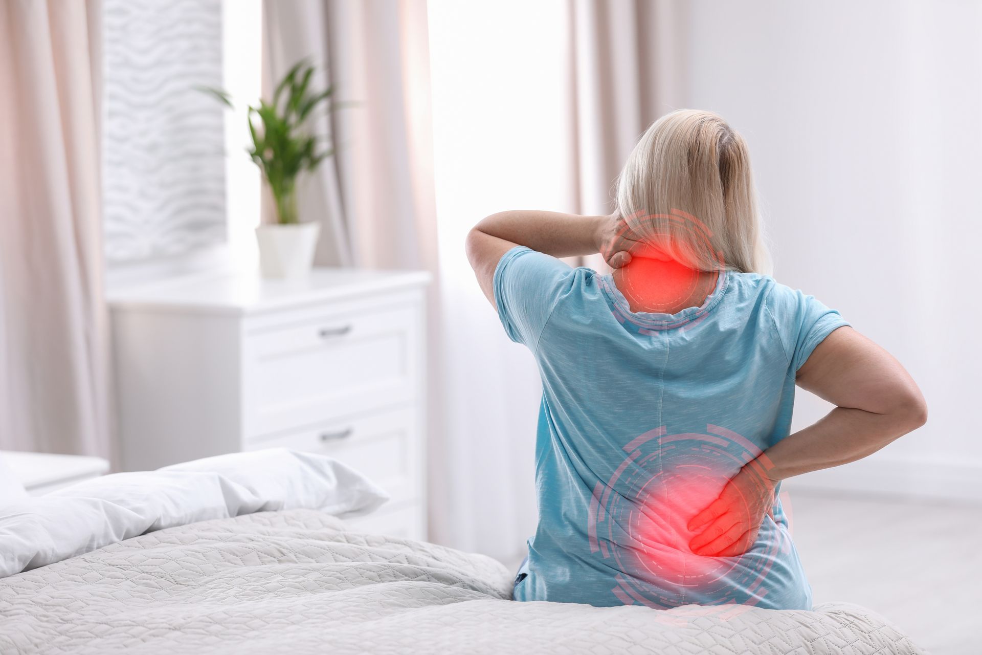 Woman in bed, holding neck and back, red circles highlight pain. Bedroom setting.
