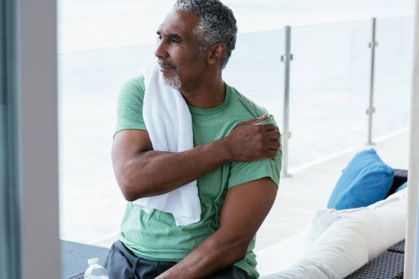 Mature man sitting on bench massaging arm due to shoulder pain after exercise.