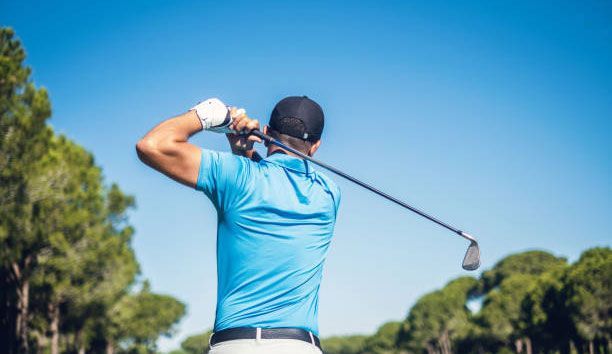 A man is swinging a golf club on a golf course.