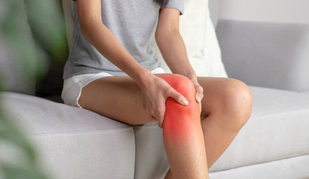 A woman is sitting on a couch holding her knee in pain.