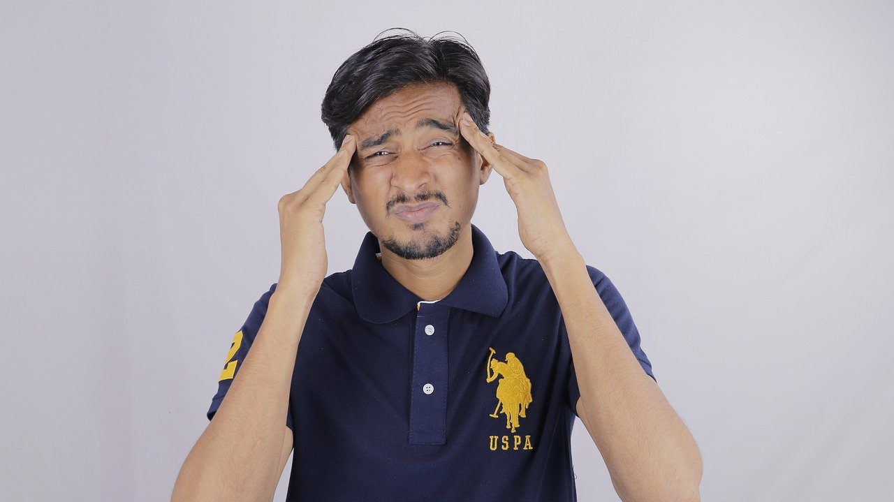 A man in a polo shirt is holding his head because he has a headache.