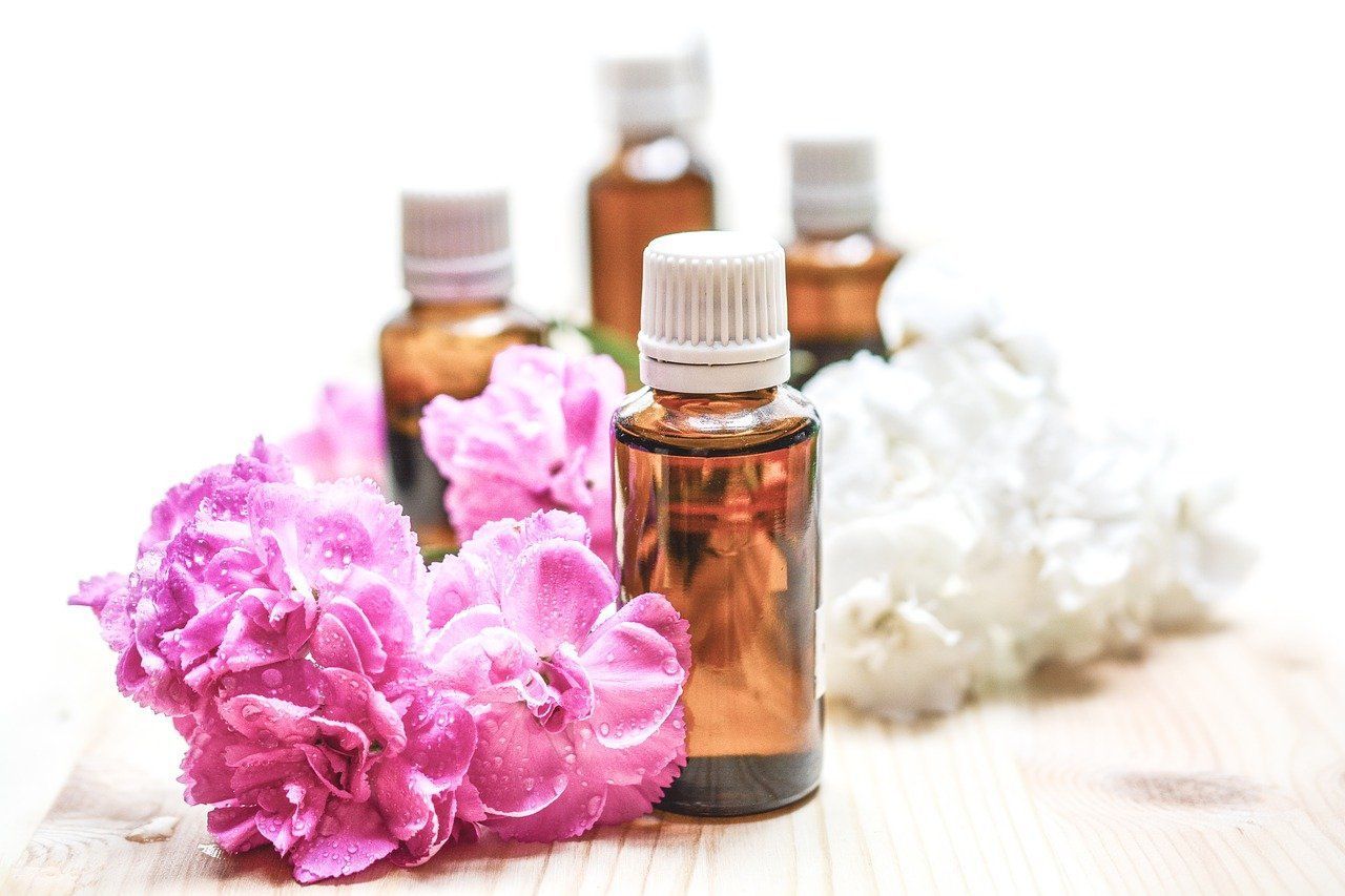 A bottle of essential oil surrounded by pink and white flowers on a wooden table.
