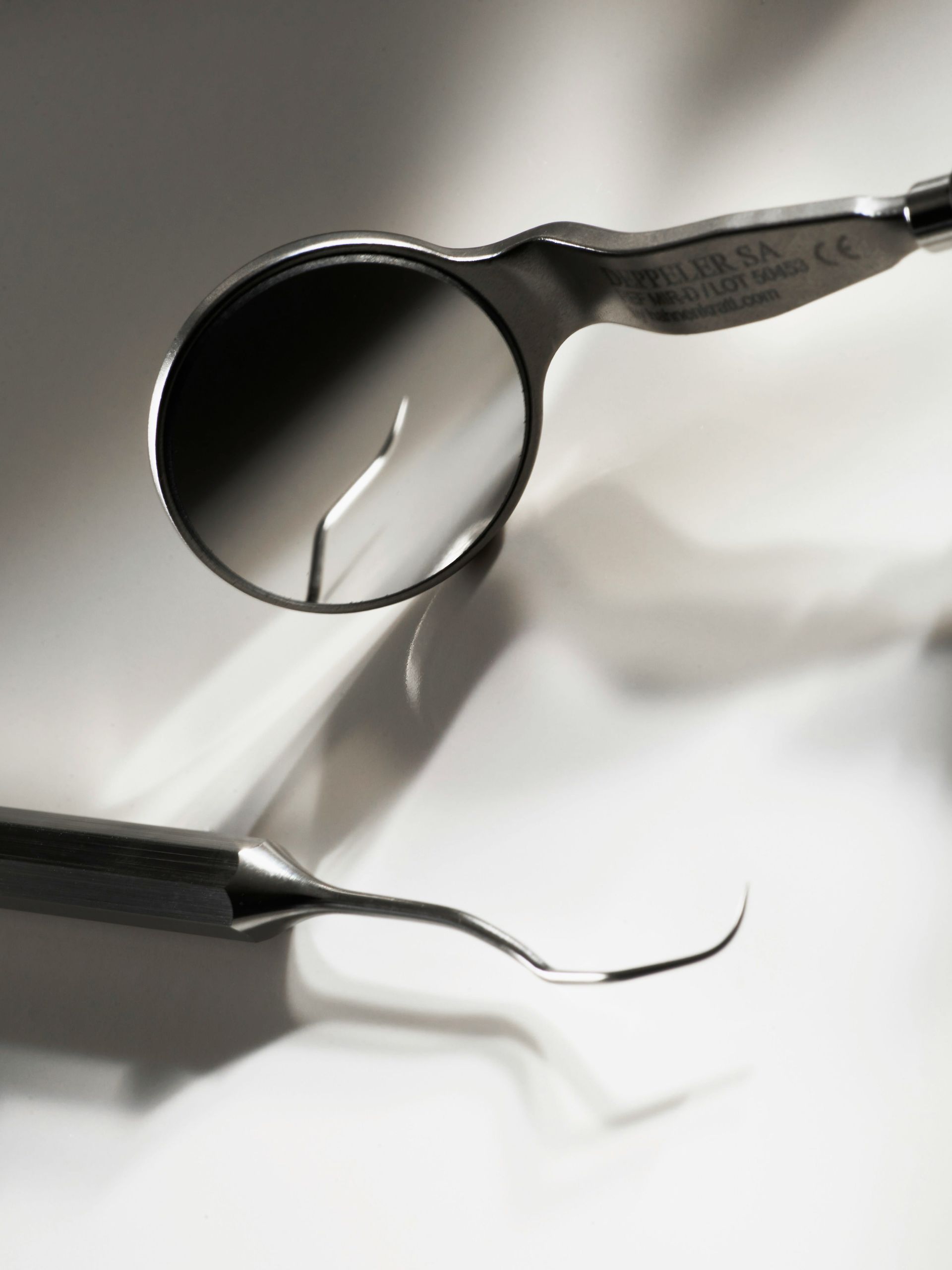 Dental mirror and explorer tool on a white surface, with slight shadows.