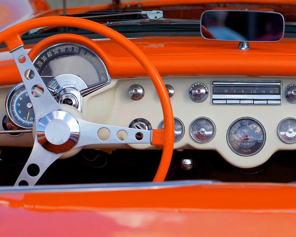 Close-up of a classic car dashboard, orange and cream colors with chrome accents, including steering wheel and gauges.