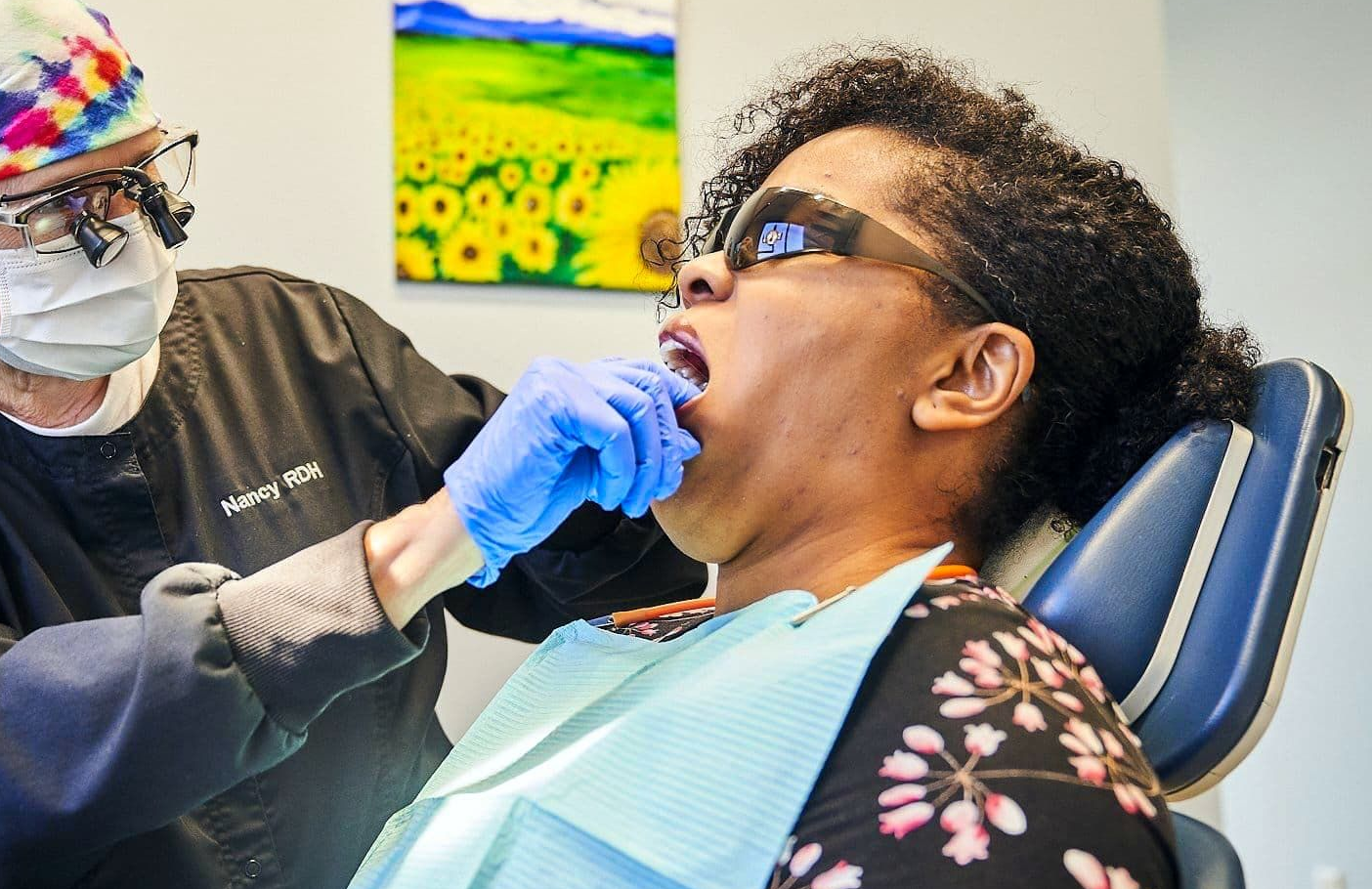 Dentist examining patient's teeth. Dentist wearing mask, gloves, and glasses. Patient has mouth open in dental chair.