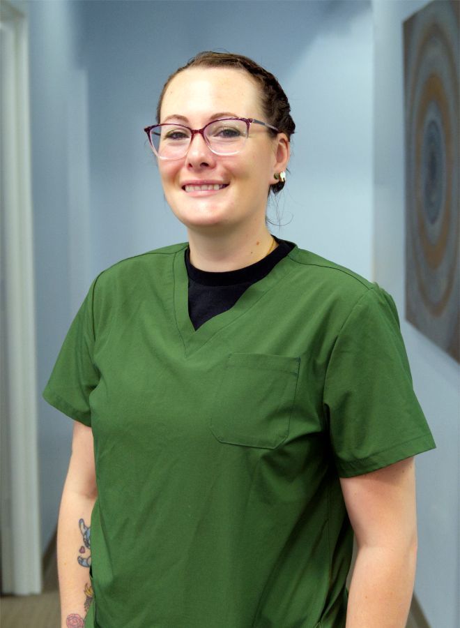 Dental office team smiles for a photo; dark scrubs, arms raised, posing near cabinets and a wall.
