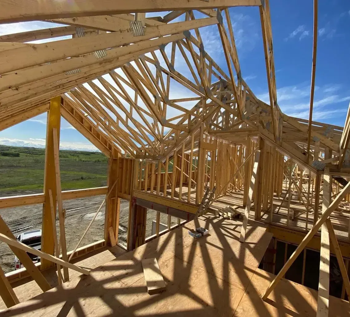 Wooden house framing under construction with exposed trusses and a blue sky overhead