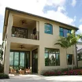 A two-story beige house with a covered patio on the first floor and a matching balcony above, featuring dark-framed windows.