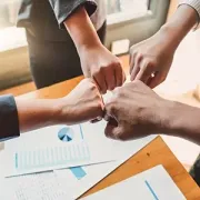 Four people performing a fist bump over a desk with business documents and charts.