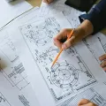 Hands in business attire review detailed technical mechanical engineering drawings on a desk.