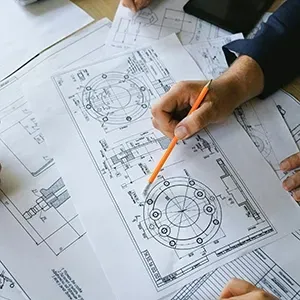 Hands in business attire review detailed technical mechanical engineering drawings on a desk.