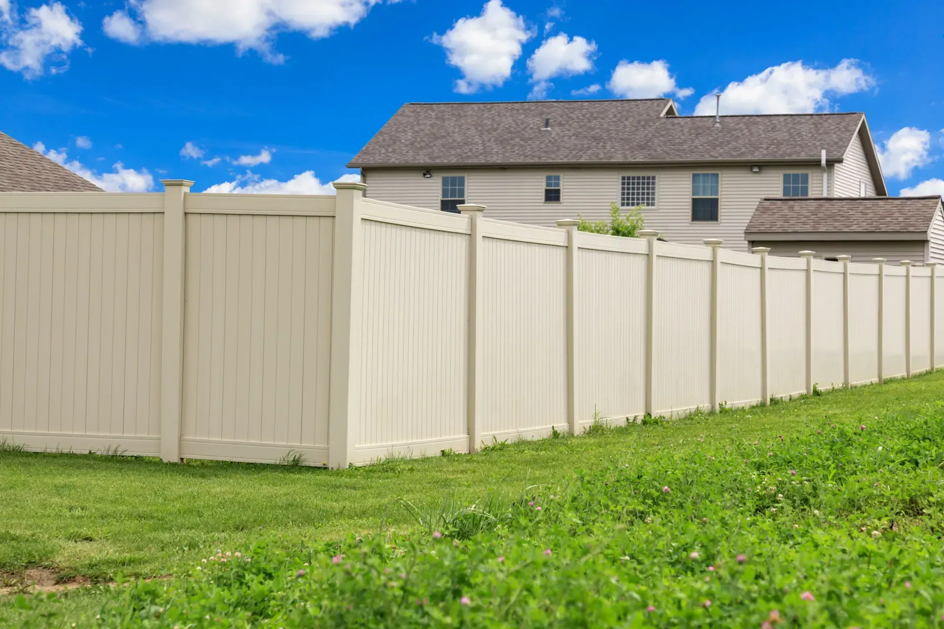 A white vinyl fence surrounds a lush green field in front of a house.
