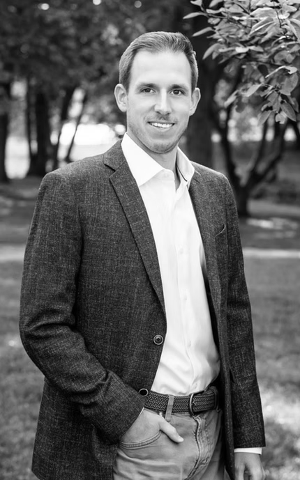 Dante Paterson. A man in a suit and white shirt is standing in a park with his hands in his pockets.