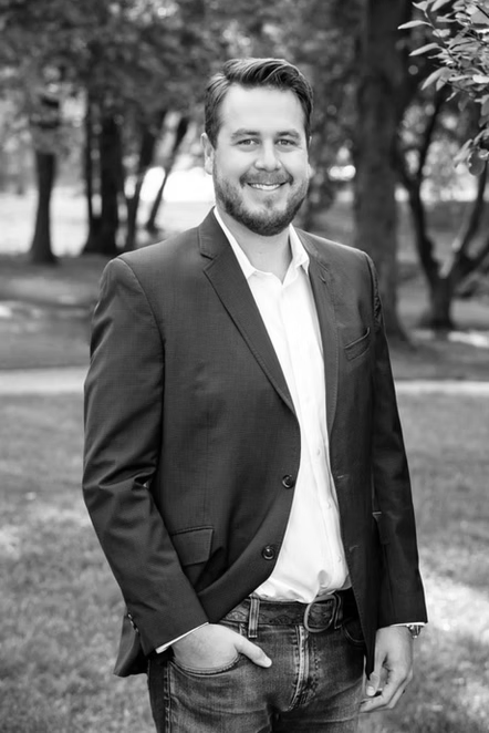 Brian Arbelaez. A man in a suit is standing in a park with his hands in his pockets.