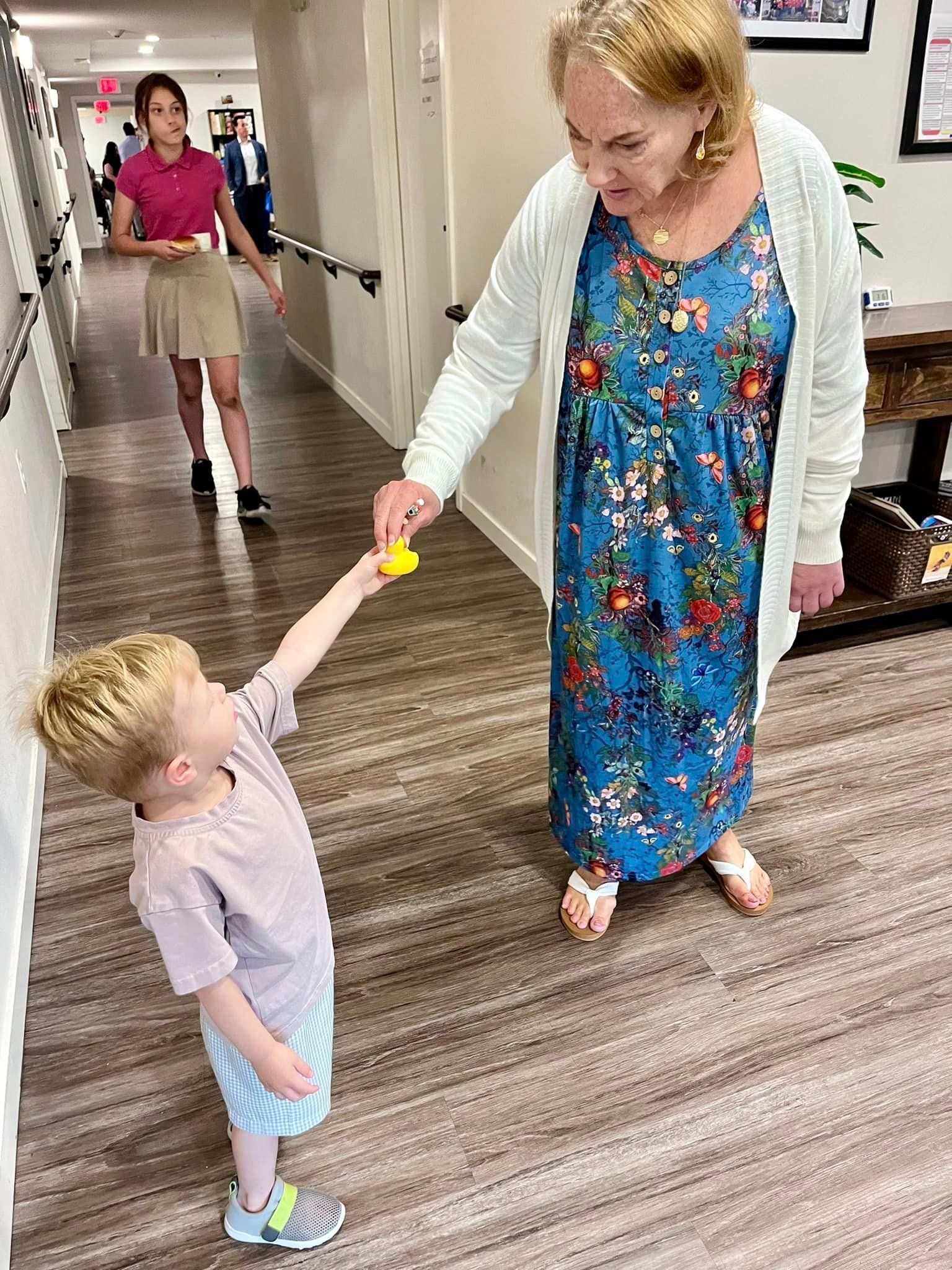 A woman is giving a yellow toy to a little boy in a hallway.