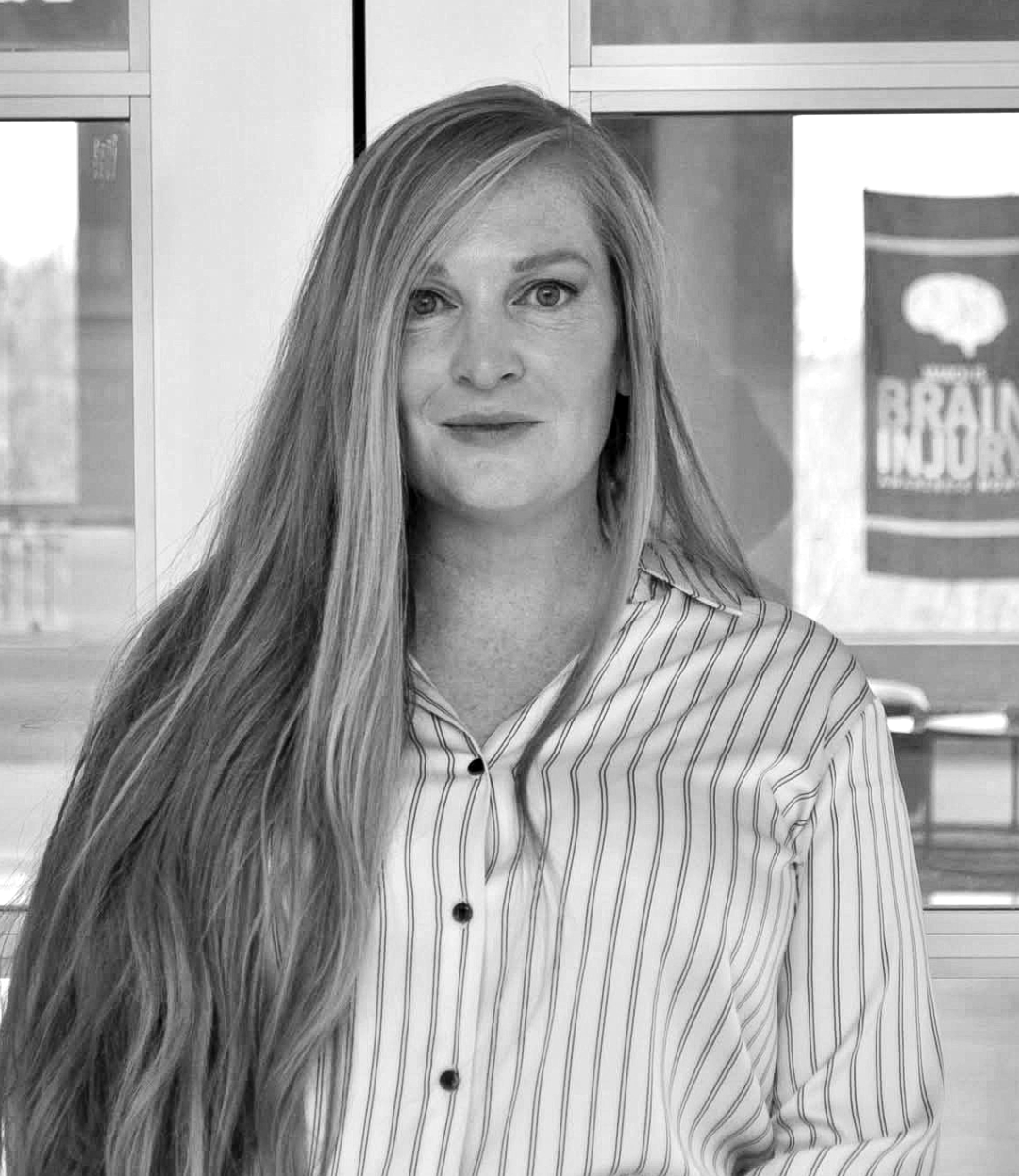 Becca Tomlin. A black and white photo of a woman with long hair wearing a striped shirt.