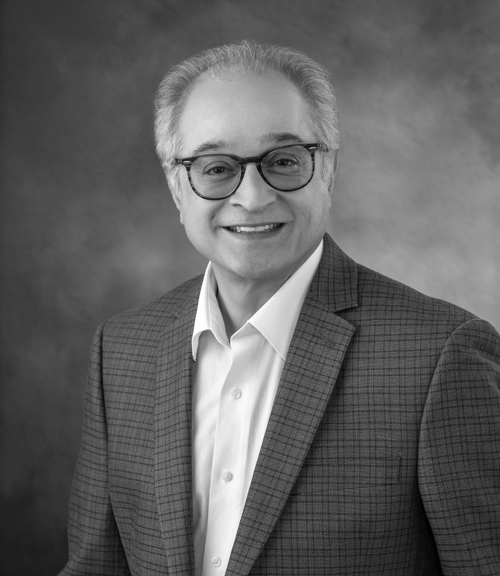 Dr. Farid Manshadi. A man in a suit and glasses is smiling in a black and white photo.