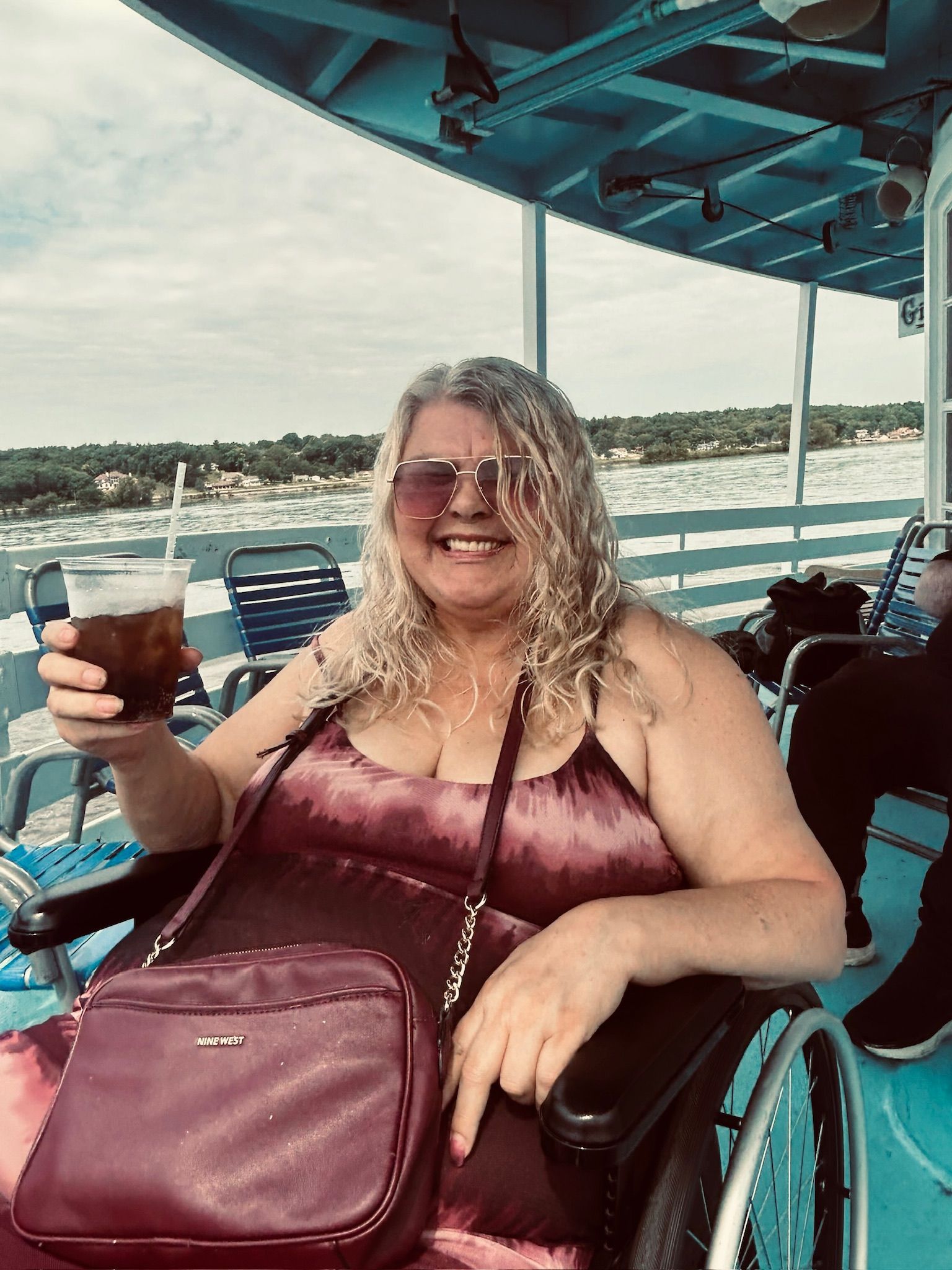 A woman in a wheelchair is sitting on a boat holding a drink.