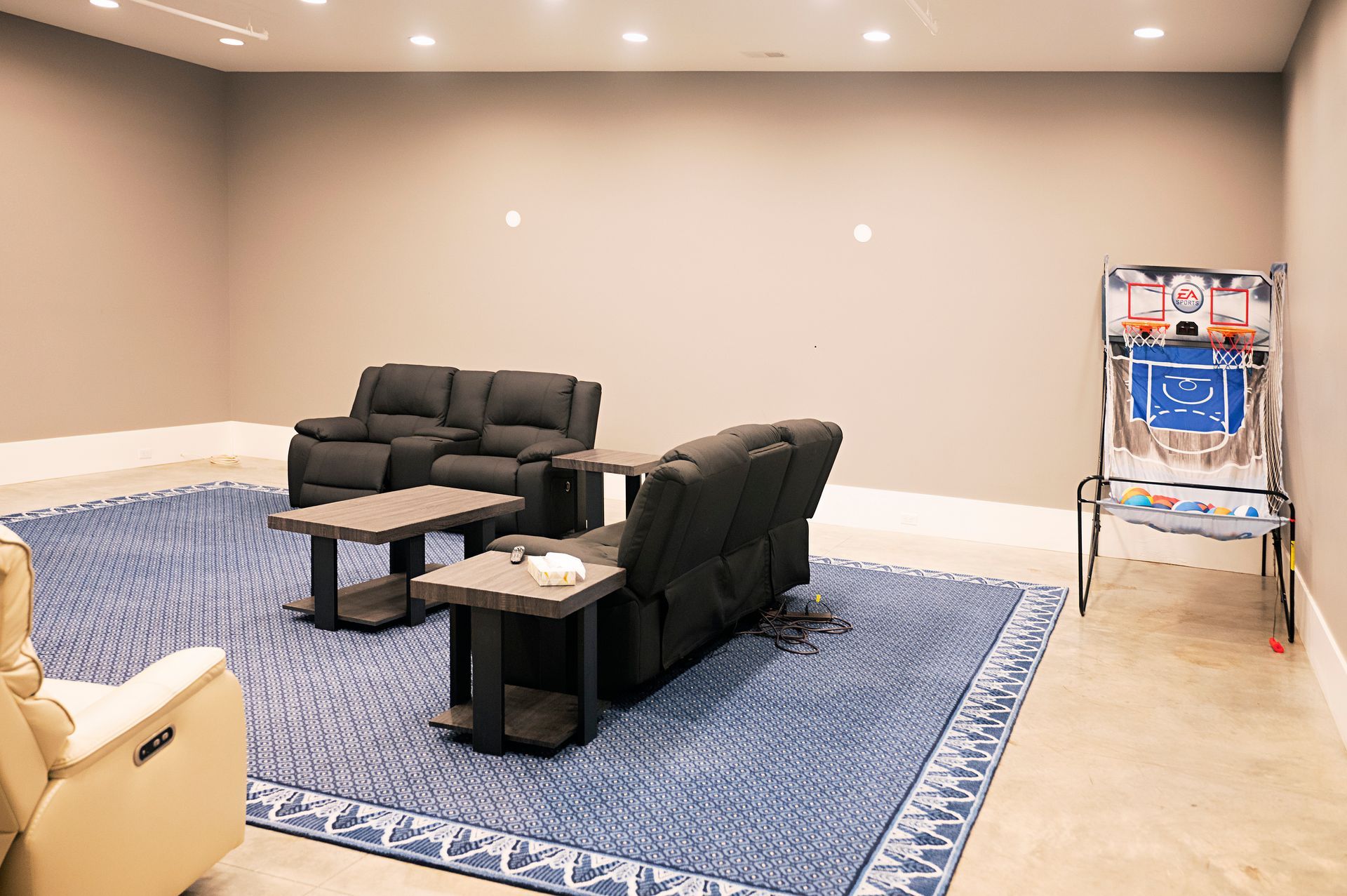 A living room with a couch , chairs , tables and a basketball game.