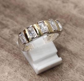 Un anillo de plata y oro se encuentra sobre un soporte de anillo blanco sobre una mesa de madera.