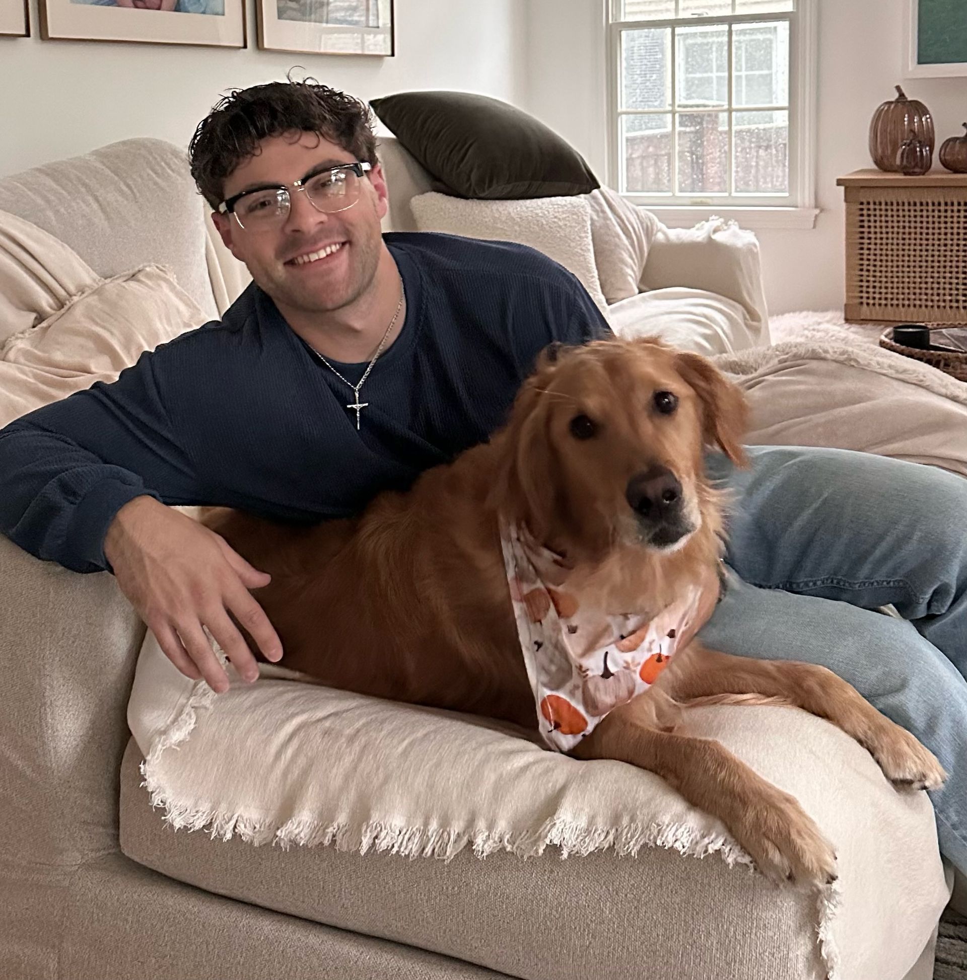 Man reclining on a sofa with a golden retriever in a bright living room.