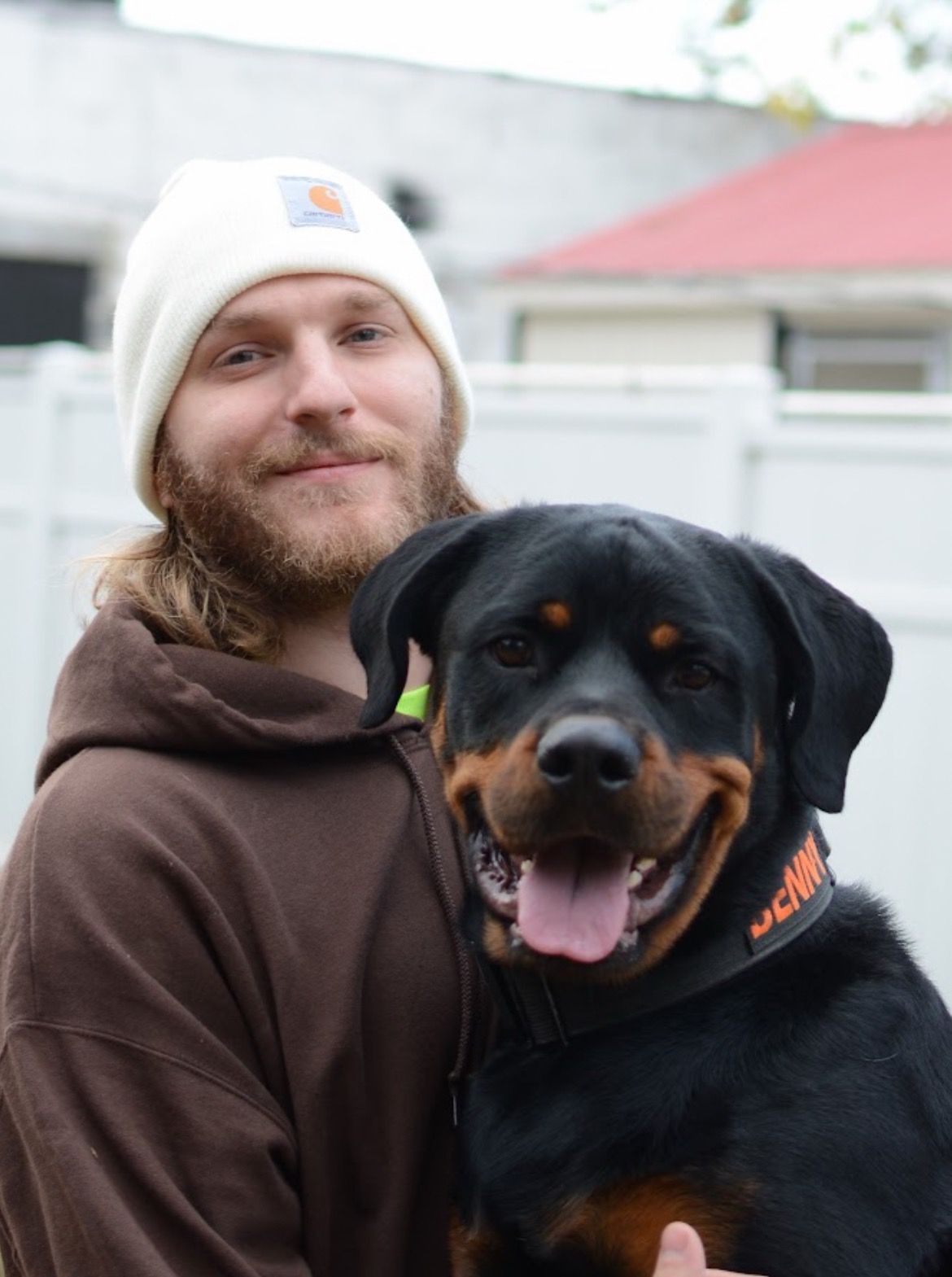 Theo holds a smiling Rottweiler dog outdoors.